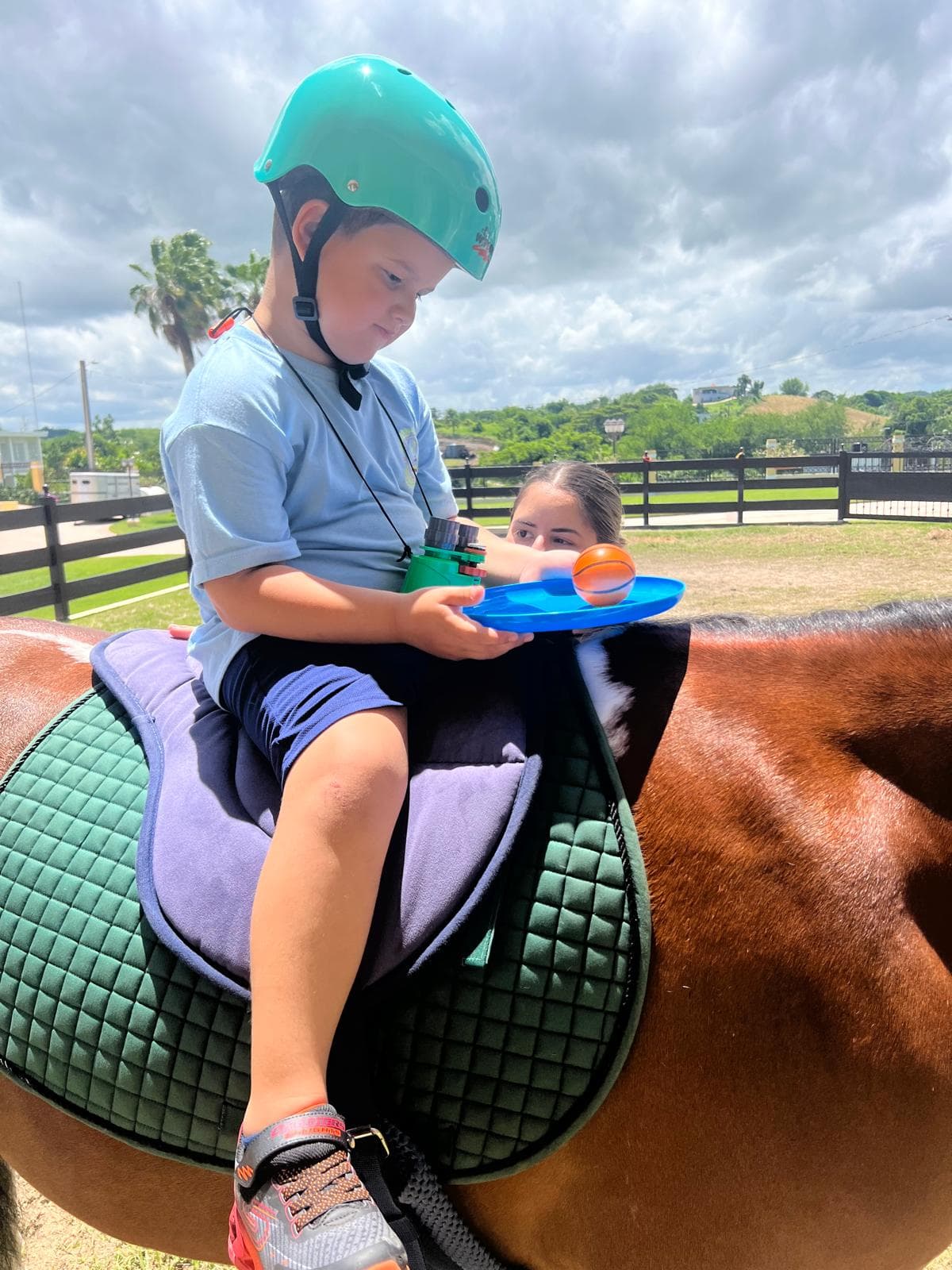 Niño montado a caballo trabajando con una bandeja sensorial junto a su terapeuta