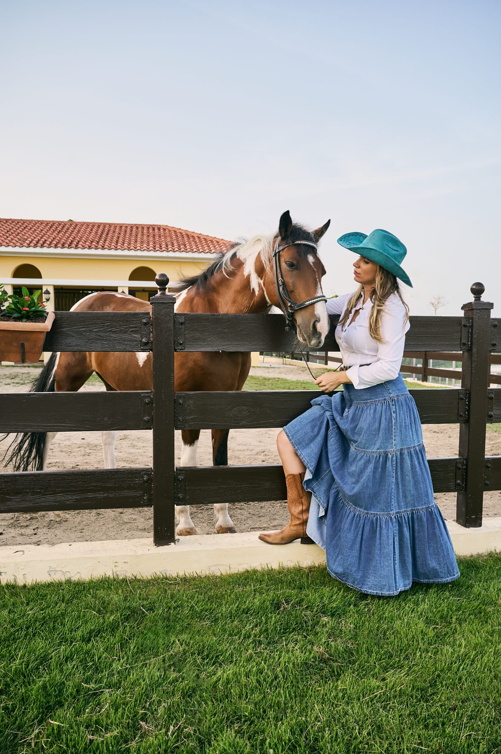 La Dra. Fabiola Najul junto a un caballo y las caballerizas de Equilibrio al atardecer
