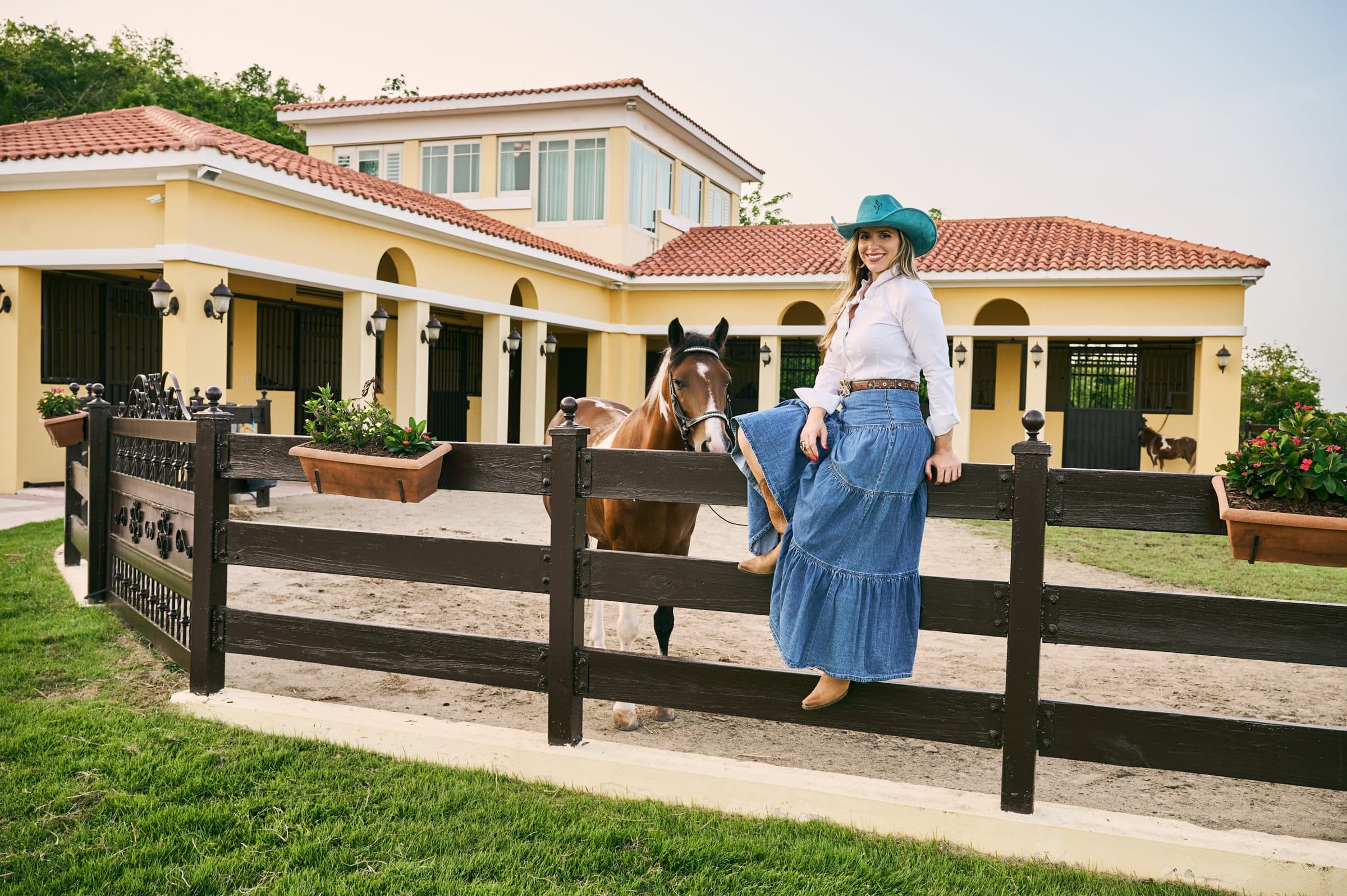 La Dra. Fabiola Najul junto a un caballo y las caballerizas de Equilibrio al atardecer
