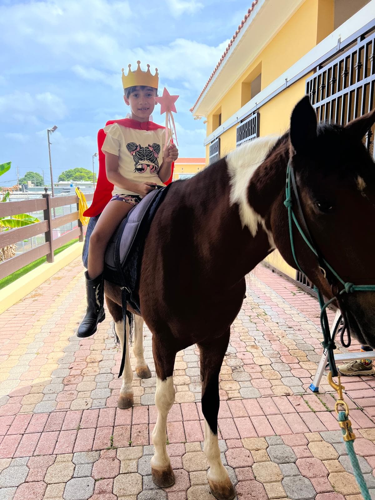 Niña con corona y capa montando un caballo durante una sesión de juego simbólico