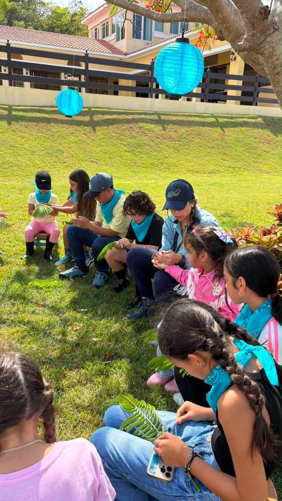 Niños sentados en la grama explorando hojas durante un taller de naturaleza