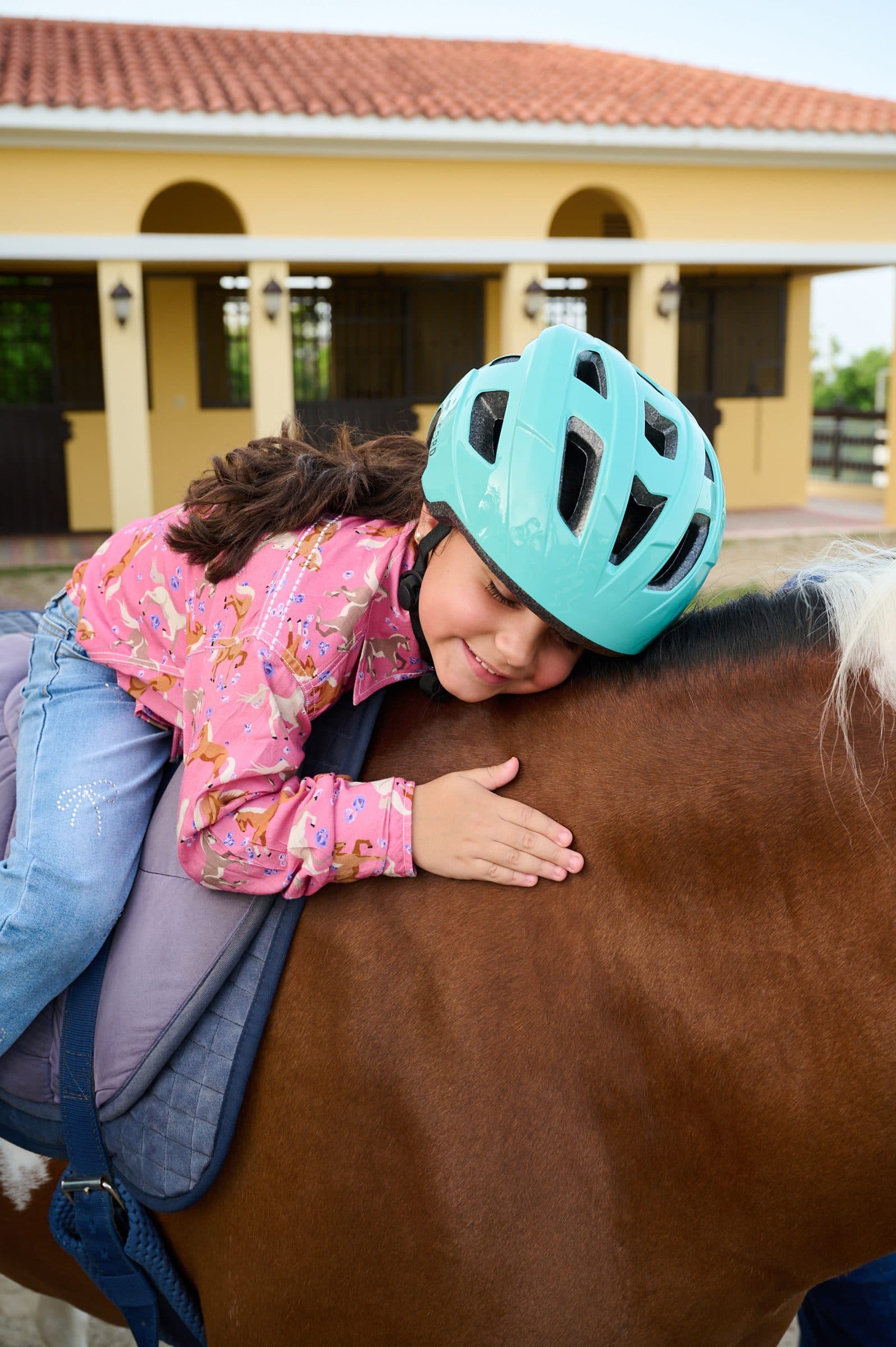 Niña con casco turquesa recostada con calma sobre el caballo