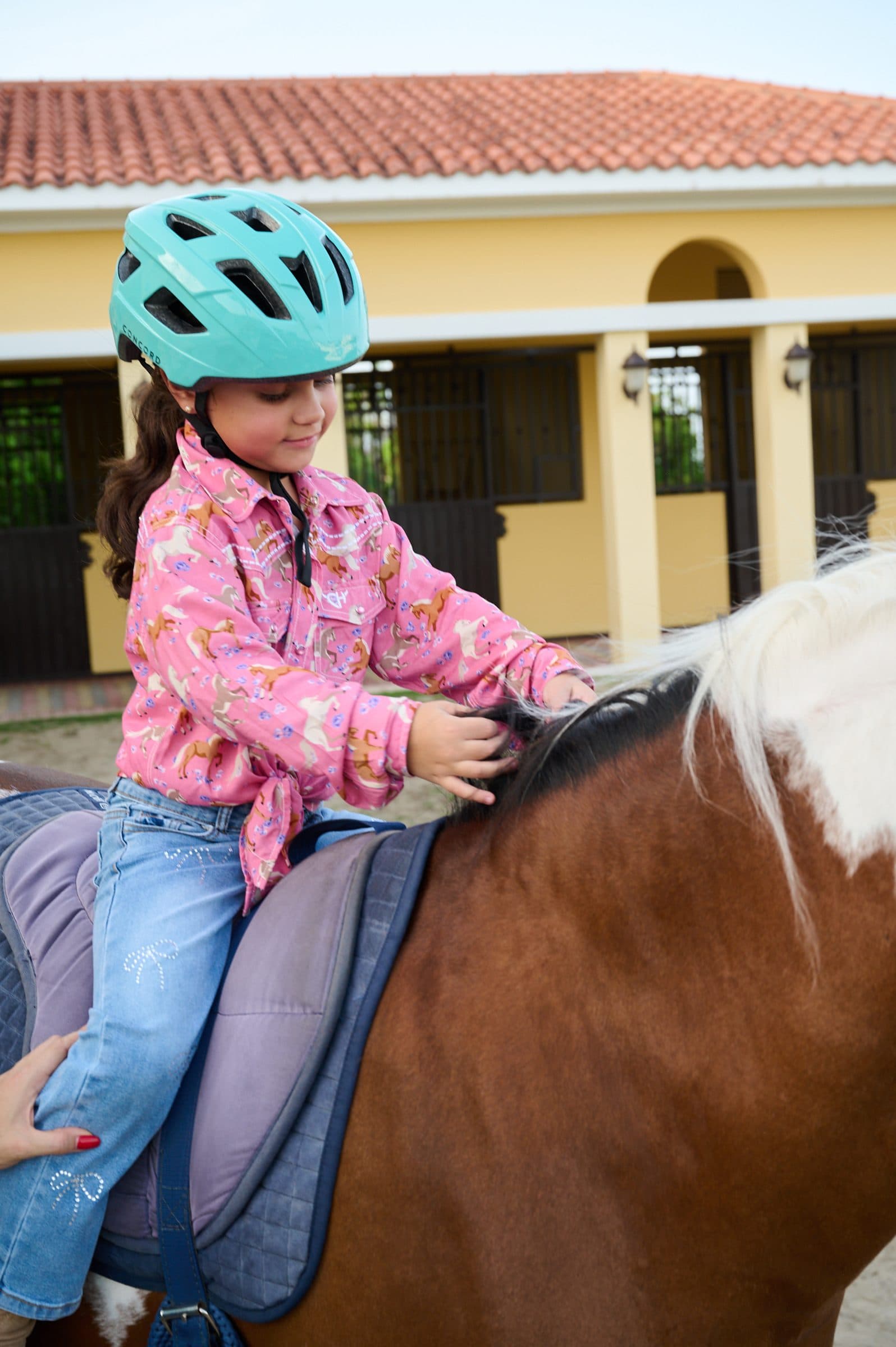 Niña con casco turquesa acariciando la crin del caballo
