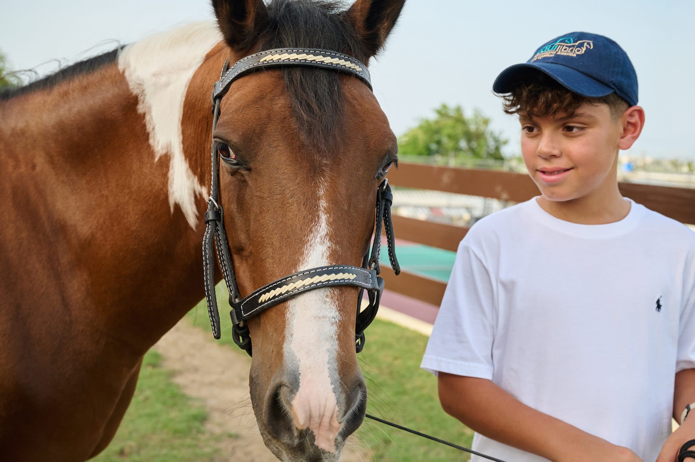 Niño con gorra junto al rostro de un caballo pinto
